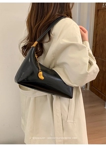 Detail of black glossy leather shoulder bag featuring irregular geometric cut and gold chain