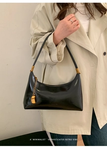 Detail of minimalist black patent leather hobo bag with gold chain and fashion pendant