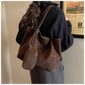 Detail of dark brown tote bag with contrast stitching and attached oval pouch charm