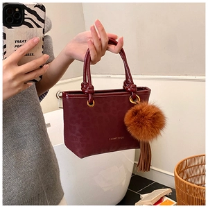 Détail du sac en cuir bordeaux avec texture animale et pendentif boule en peluche