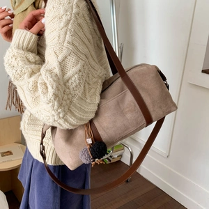 Detalle de bolso Boston de ante caqui con asas de cuero marrón y colgante de piel gris
