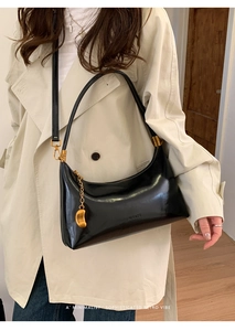Detail of black glossy leather shoulder bag with gold crescent moon charm and logo
