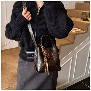 Detail of dark brown crocodile-embossed bucket bag with fringe and cartoon charm detail