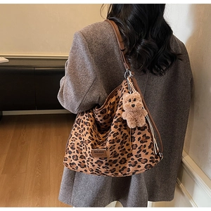 Detail of leopard print tote bag with brown leather straps and plush bear charm