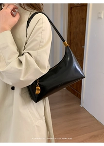 Detail of retro black leather underarm bag featuring a gold fashion pendant and brand logo