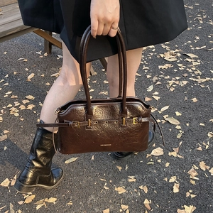 Deep brown textured leather tote bag with gold buckle and straps on autumn leaves