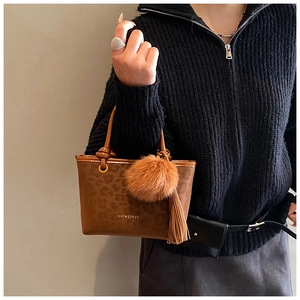 Détail du sac à main marron imprimé léopard avec pompon en peluche et logo