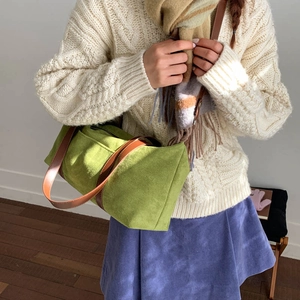 Detalle de bolso cilíndrico de ante verde con asas marrones en una modelo