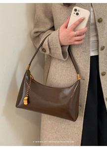 Detail of dark brown glossy leather baguette bag with a gold crescent charm on the side