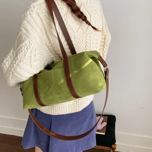 Bolso tipo almohada de ante verde con correa marrón sobre un suéter de punto