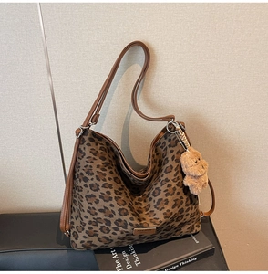 Detail of leopard print tote bag with brown leather handles and a plush bear pendant