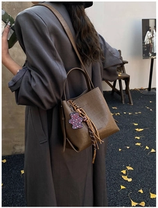 Detail of dark brown crocodile-embossed bucket bag with heart bear charm and fringe