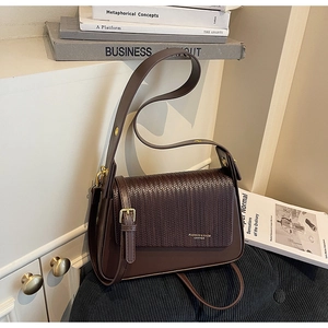Detail of dark brown leather bag showing woven flap texture and gold hardware accents