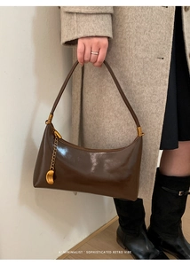 Detail of a vintage dark brown baguette bag with gold chain charm on a wool coat