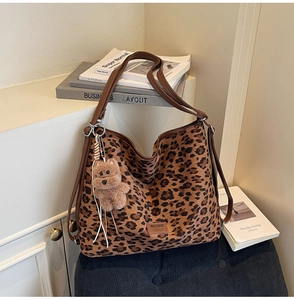 Detail of leopard print tote bag with brown leather handles and a plush bear charm