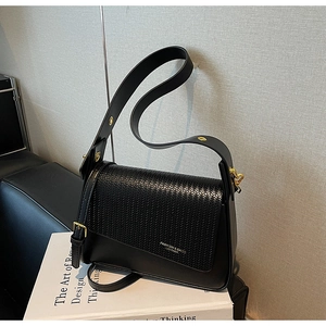 Detailed view of black woven flap texture on a square shoulder bag with gold hardware