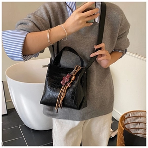Detail of black crocodile texture bucket bag with top handle and bear charm accent