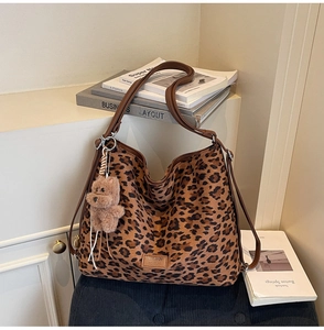 Close-up of leopard print tote bag with brown leather strap and plush bear charm