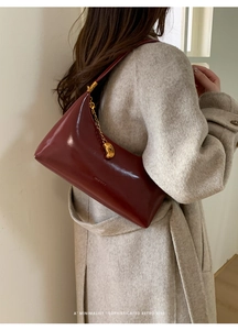 Detail of burgundy glossy leather baguette bag with gold chain worn on wool coat