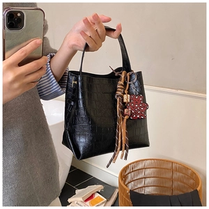 Detail of black crocodile texture bucket bag with bear pendant and woven tassel charm