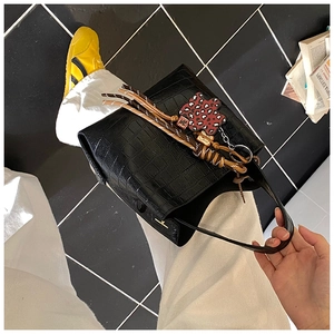 Detail of black crocodile embossed bucket bag with red leopard flower pendant charm