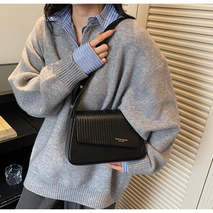Detail of black leather underarm bag featuring a woven textured flap and gold lettering