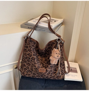 Detail of leopard print tote bag with brown leather handles and cute plush bear keychain