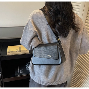Detail of black leather and woven shoulder bag featuring an asymmetric flap and gold logo
