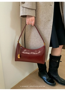 Detail of burgundy baguette bag featuring a shiny finish and gold heart pendant