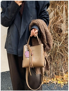 Detail of tan crocodile-pattern bucket bag with woven tassel and leopard bear charm