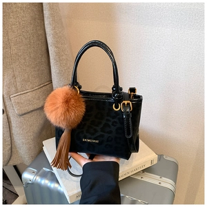 Détail du sac seau léopard noir avec logo doré et accessoire pompon en peluche