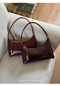 Detail of wine red patent leather baguette bag with gold moon pendant on a sofa