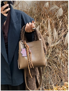 Close-up of brown crocodile pattern bucket bag with colorful tassels and bear charm