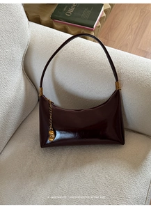 Close-up of a retro burgundy patent leather hobo bag with gold hardware on a sofa