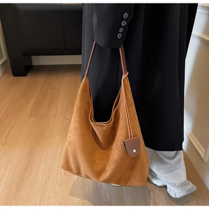 Detail of a large brown suede tote bag featuring a leather strap and side pendant