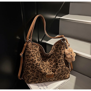 Detailed view of leopard print tote bag with brown leather straps and plush bear charm