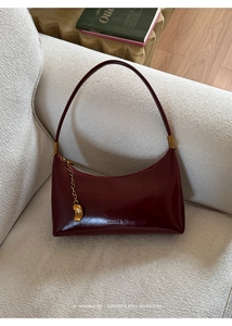 Detail of vintage burgundy leather shoulder bag with gold bean pendant on beige sofa
