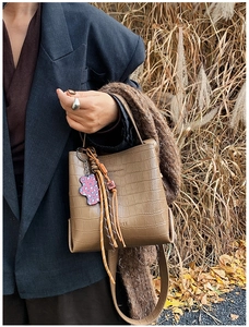 Close-up of brown crocodile texture bucket bag with purple bear and tassel details