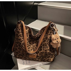 Detail of leopard print tote bag with brown leather handles and plush bear charm