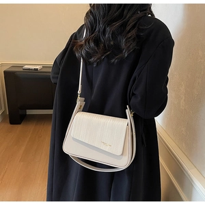 Detail of cream-colored shoulder bag featuring a woven texture flap and gold lettering