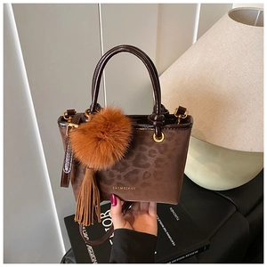 Détail du sac à main marron foncé à motif léopard avec pompon en peluche et glands