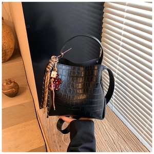 Detail of black crocodile texture bucket bag with vintage bear and tassel charm accessory