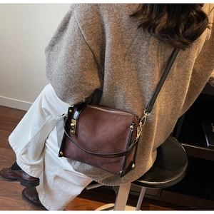 Detail of a dark brown quilted crossbody bag with gold hardware and contrast black piping