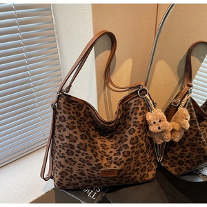 Detailed view of leopard print tote bag with brown leather strap and plush bear charm