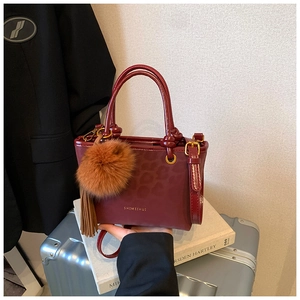 Détail du sac seau bordeaux avec gaufrage léopard, pompon en fourrure et franges