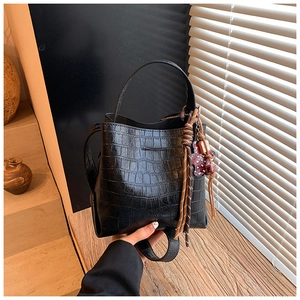 Close-up of black crocodile-embossed bucket bag with cute bear charm and woven knot detail