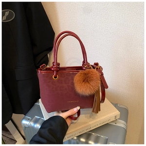 Gros plan détaillé du sac seau bordeaux avec texture léopard gaufrée et pompon décoratif