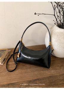Detail of a vintage black leather bag with gold accents and a decorative bean charm