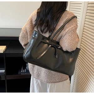 Detail shot of a black oversized tote bag with decorative straps and metal rings