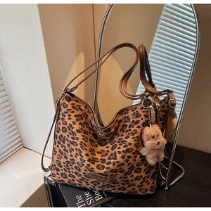 Detail view of leopard print tote bag with brown straps and plush bear charm accent